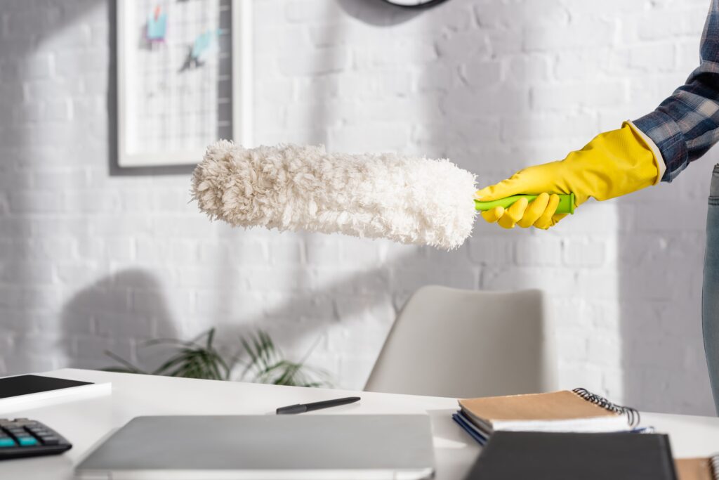 Reinigungskraft mit gelben Handschuhen staubt im Büro einen Schreibtisch mit Laptop ab – ein Symbolbild für Polarglanz Unterhaltsreinigung Hamburg, Reinigungsfirma für Büros