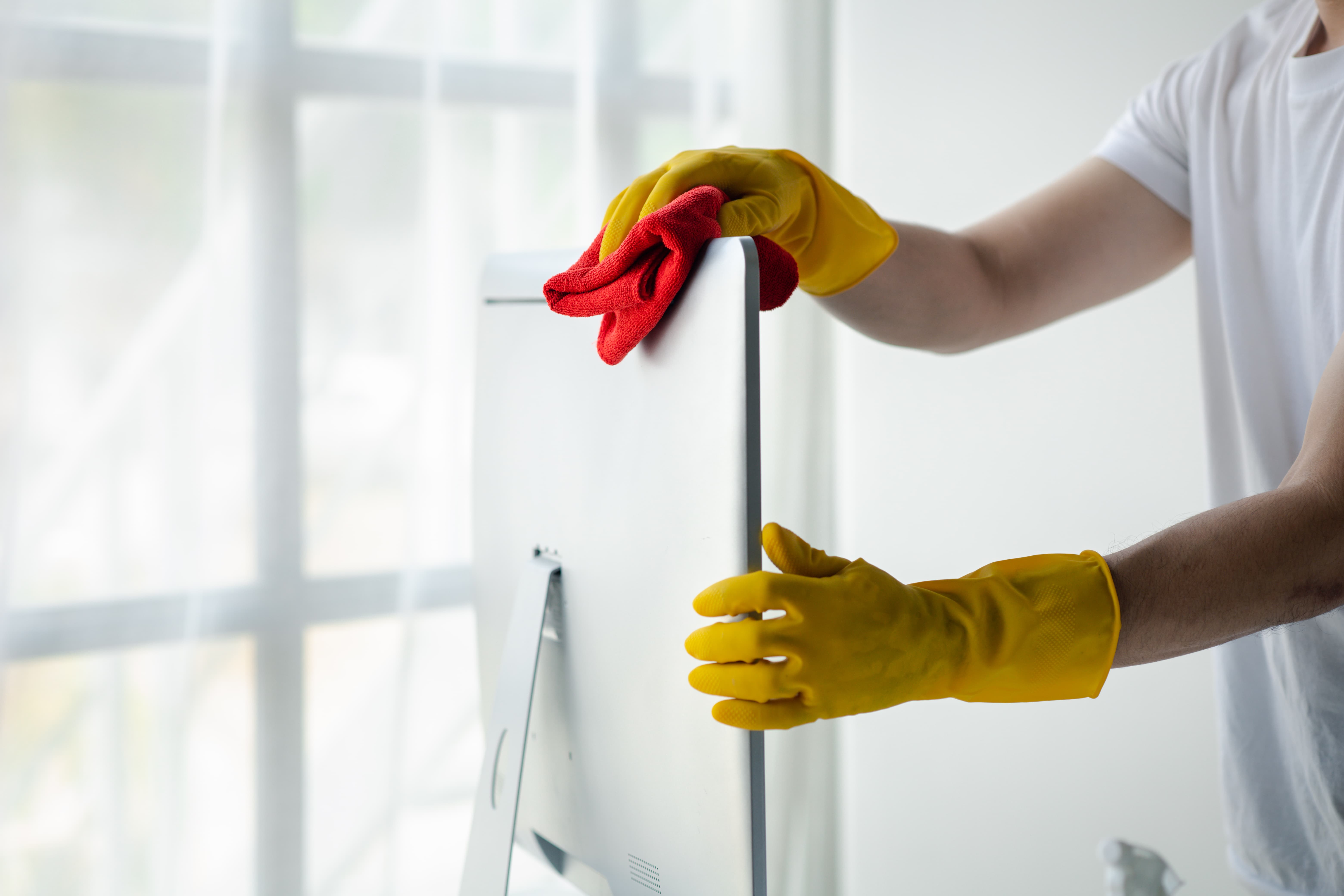 Reinigungskraft mit gelben Handschuhen wischt einen Bildschirm in einem modernen Büro – professionelle Büroreinigung in Hamburg für hygienische Arbeitsplätze.
