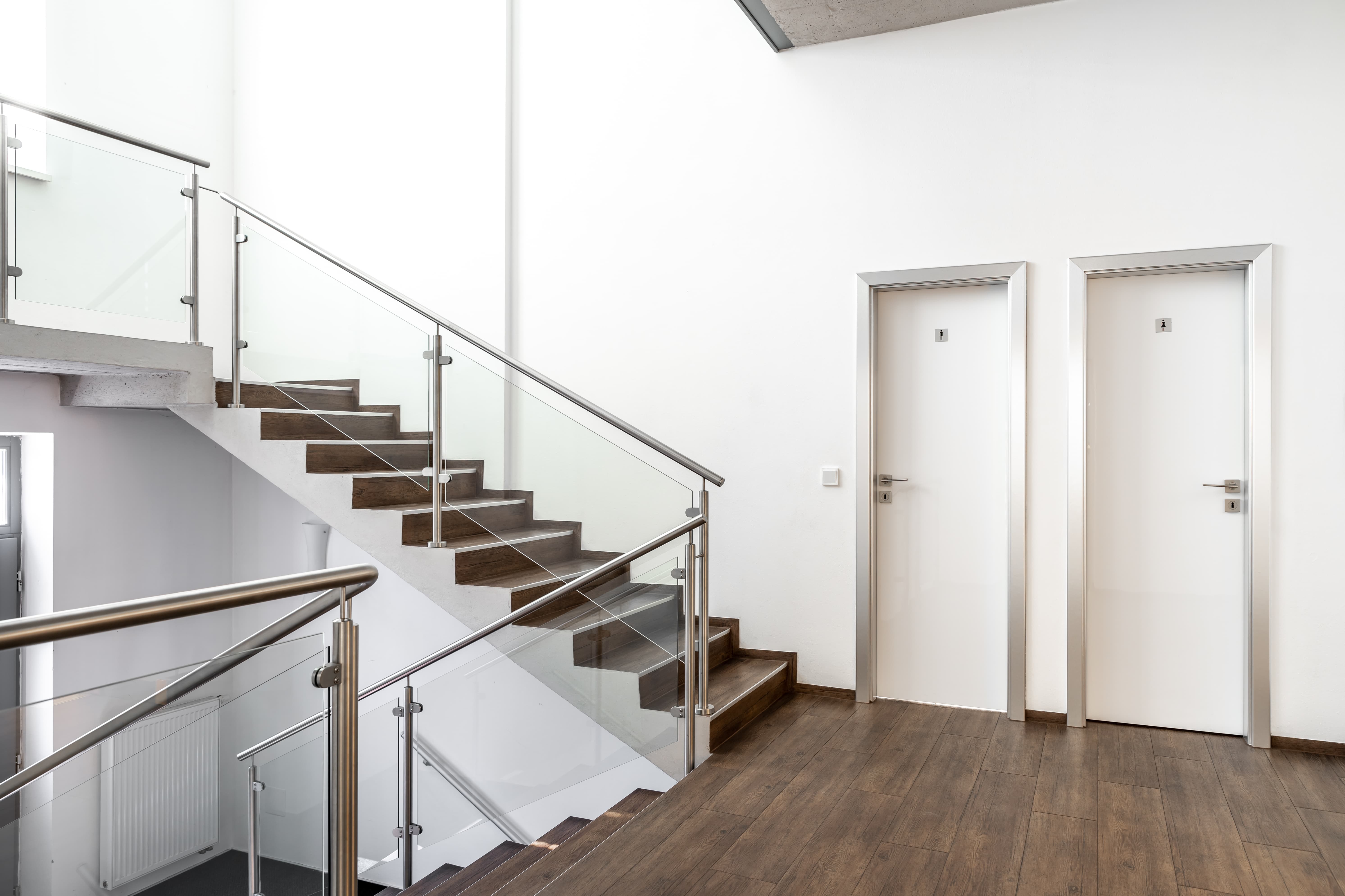 Modernes Treppenhaus mit Holzstufen, weißen Wänden und Glasgeländern – Polarglanz Treppenhausreinigung in Hamburg für gepflegte und saubere Eingangsbereiche.