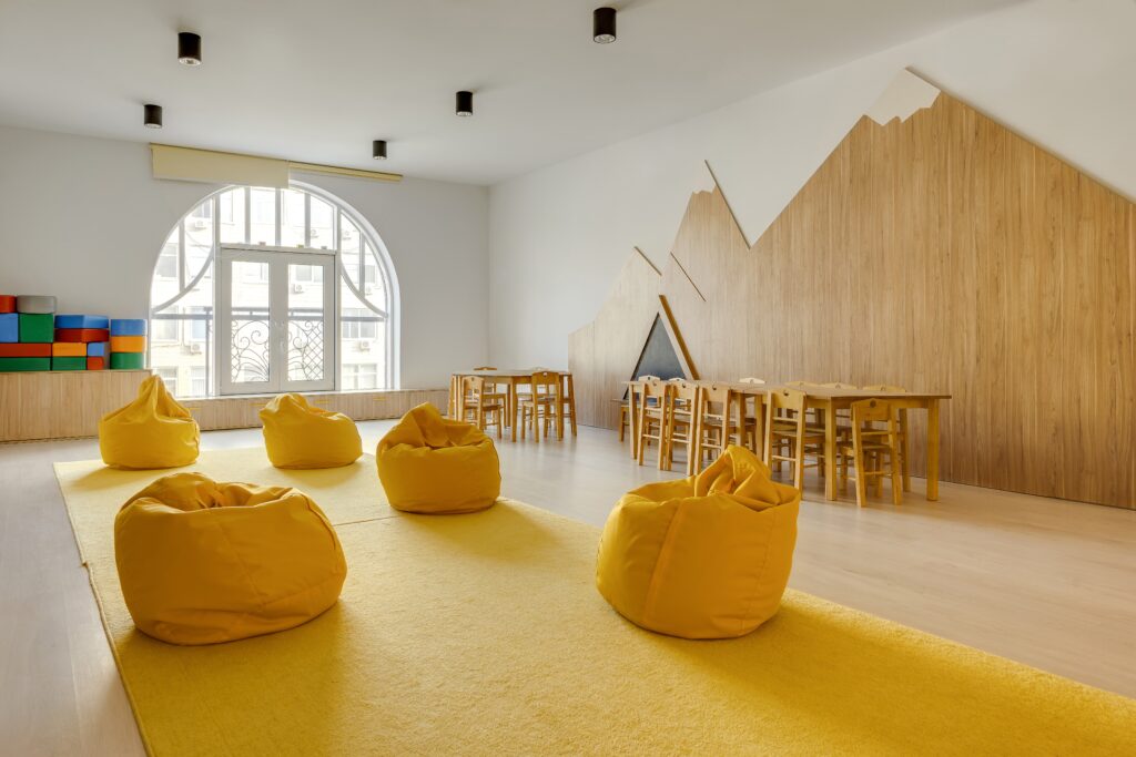 Moderner Kindergartenraum mit gelbem Teppich, Sitzsäcken und Holzmöbeln – Symbol für regelmäßige und gründliche Kita- und Schulreinigung in Hamburg.